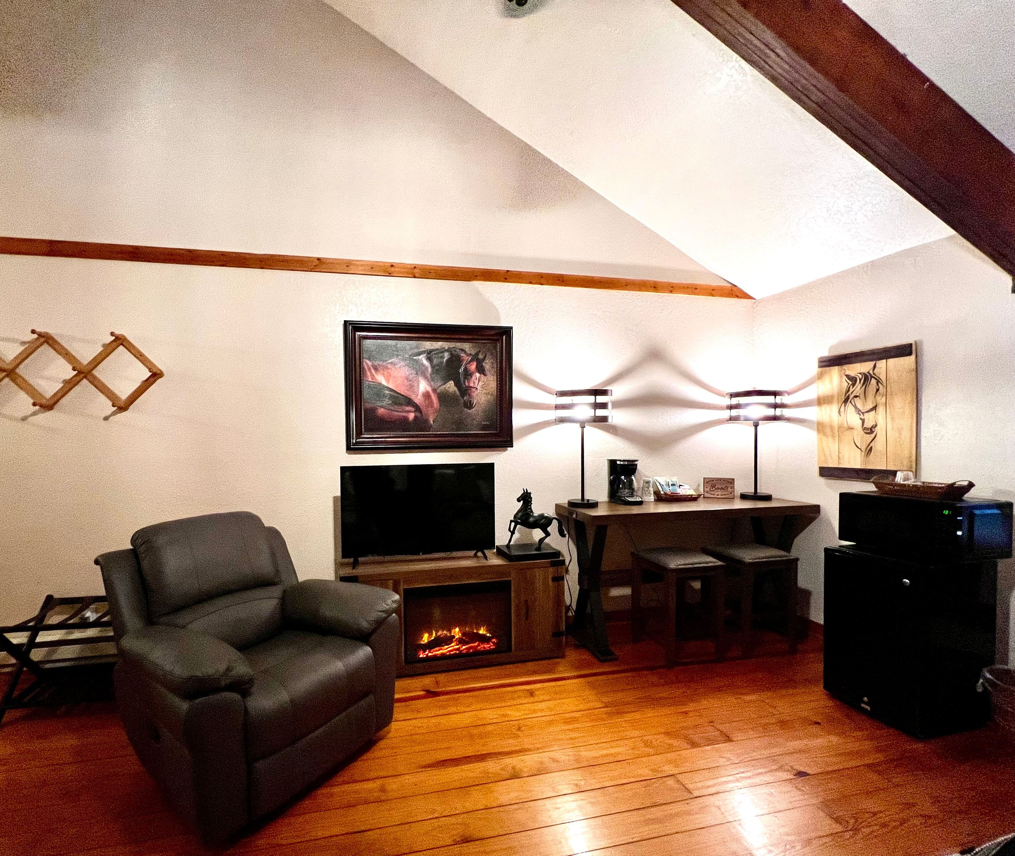 Cozy sitting area with large leather recliner, electric fireplace, flat-screen TV, and coffee bar with stools