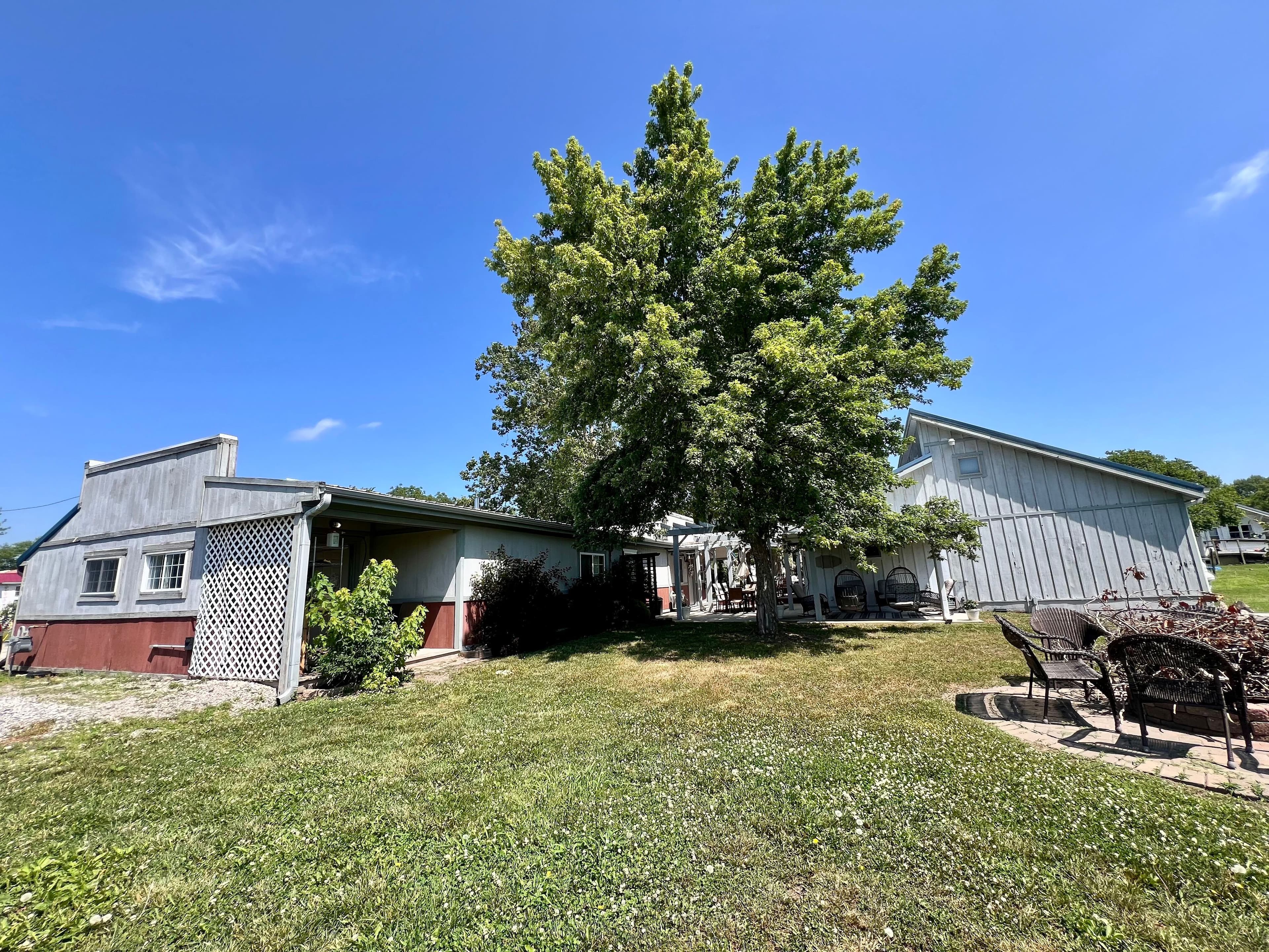 View behind buildings, yard, and seating area with green grass, trees, and bright blue sky