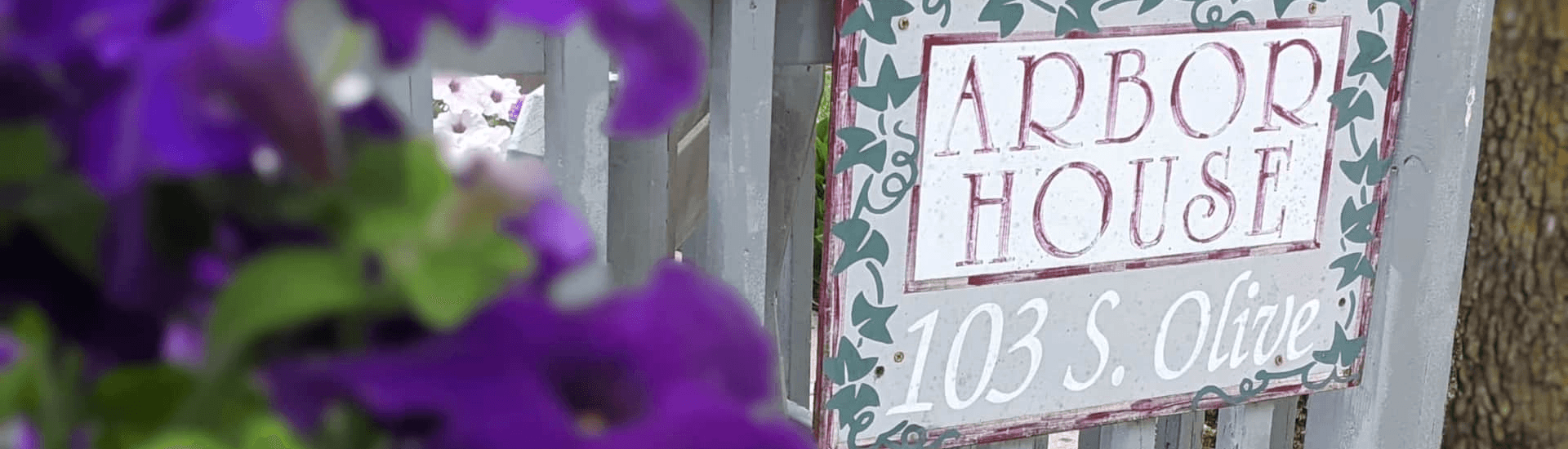 Purple flowers in front of railing with a sign for Arbor House attached to the railing.