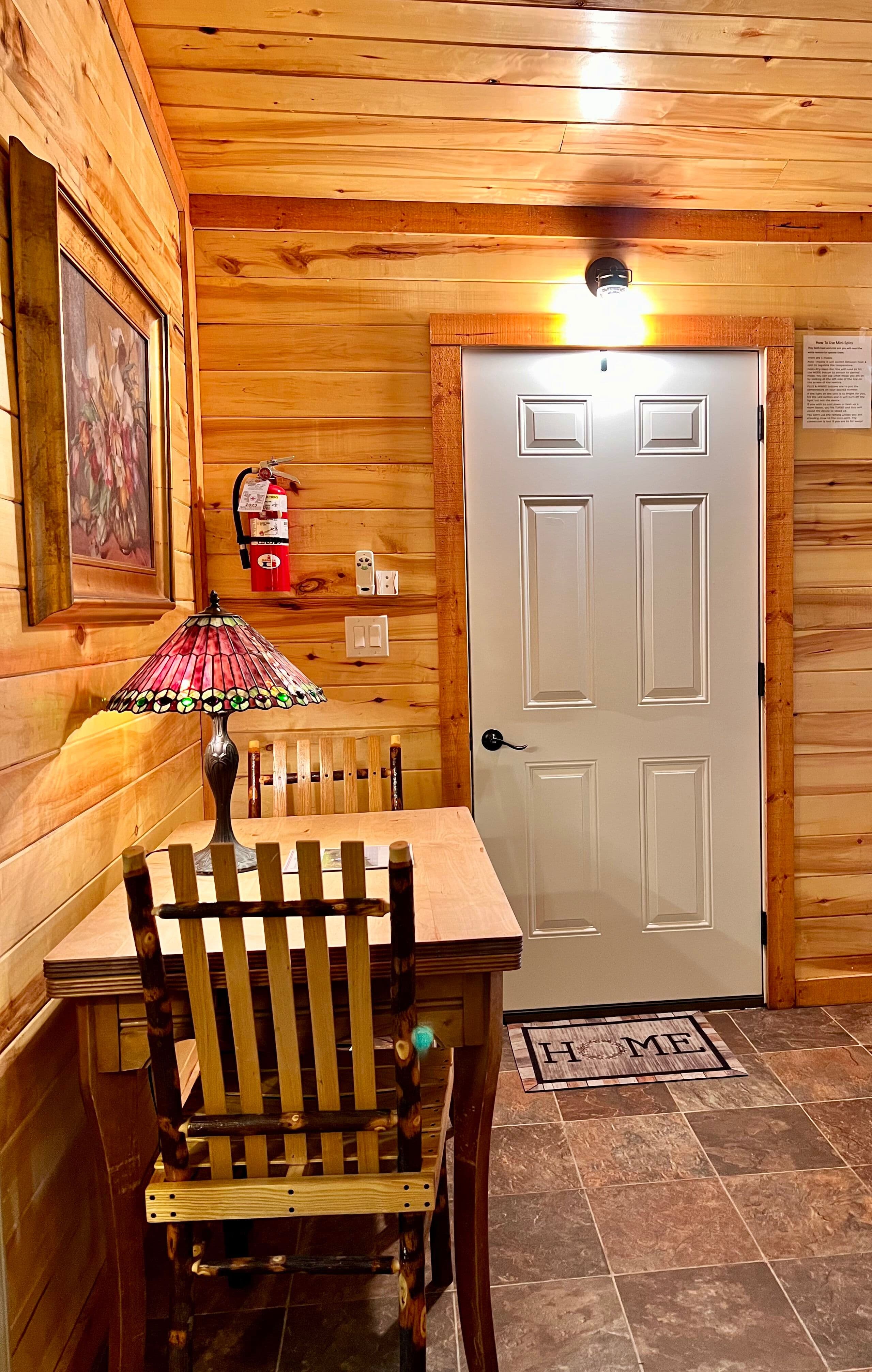 Table and chairs for two with Tiffany-style lamp, natural wood walls and ceiling, white door leading to outside