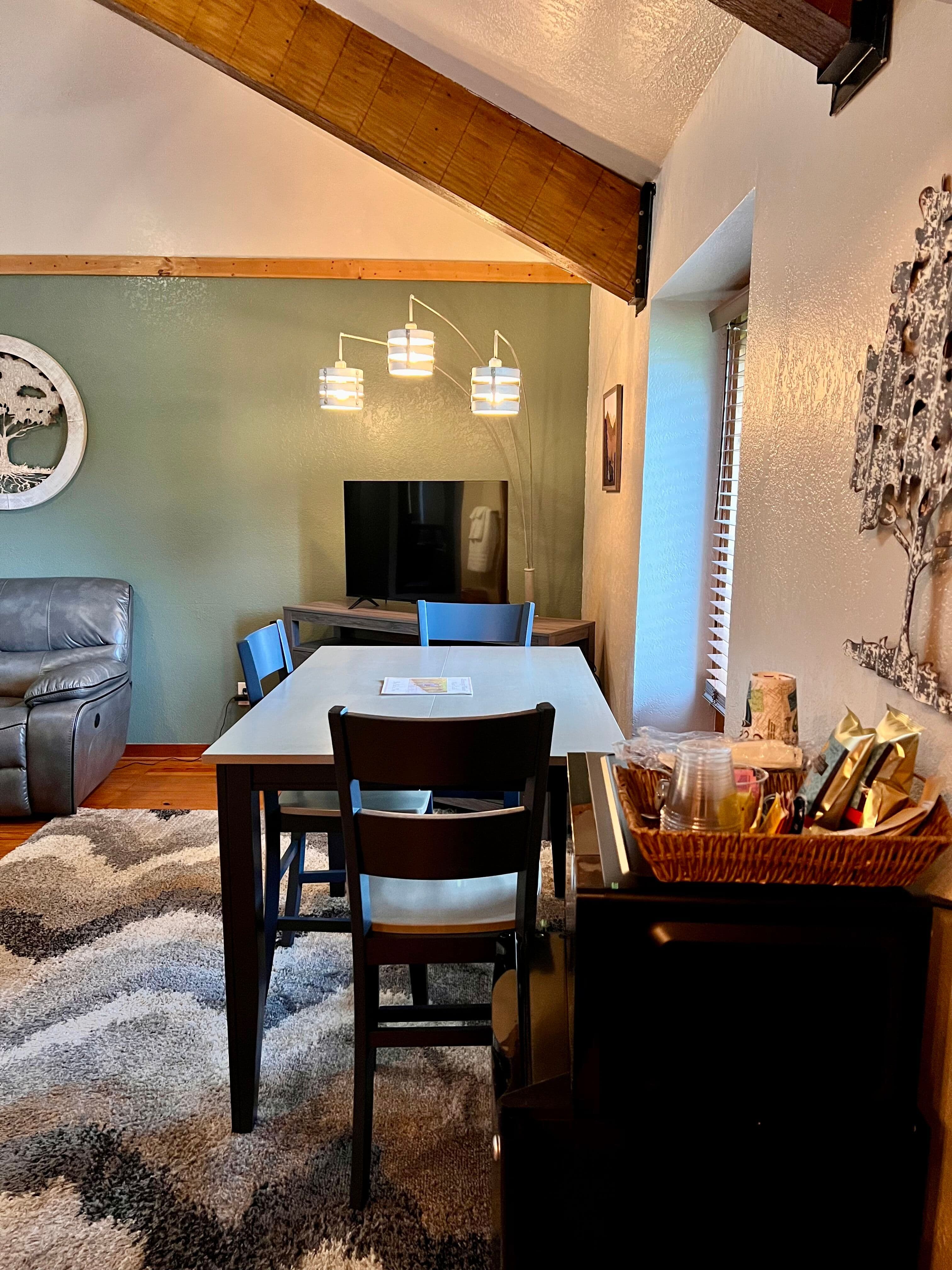 Coffee bar in foreground, dining table with chairs next to window, TV center in background
