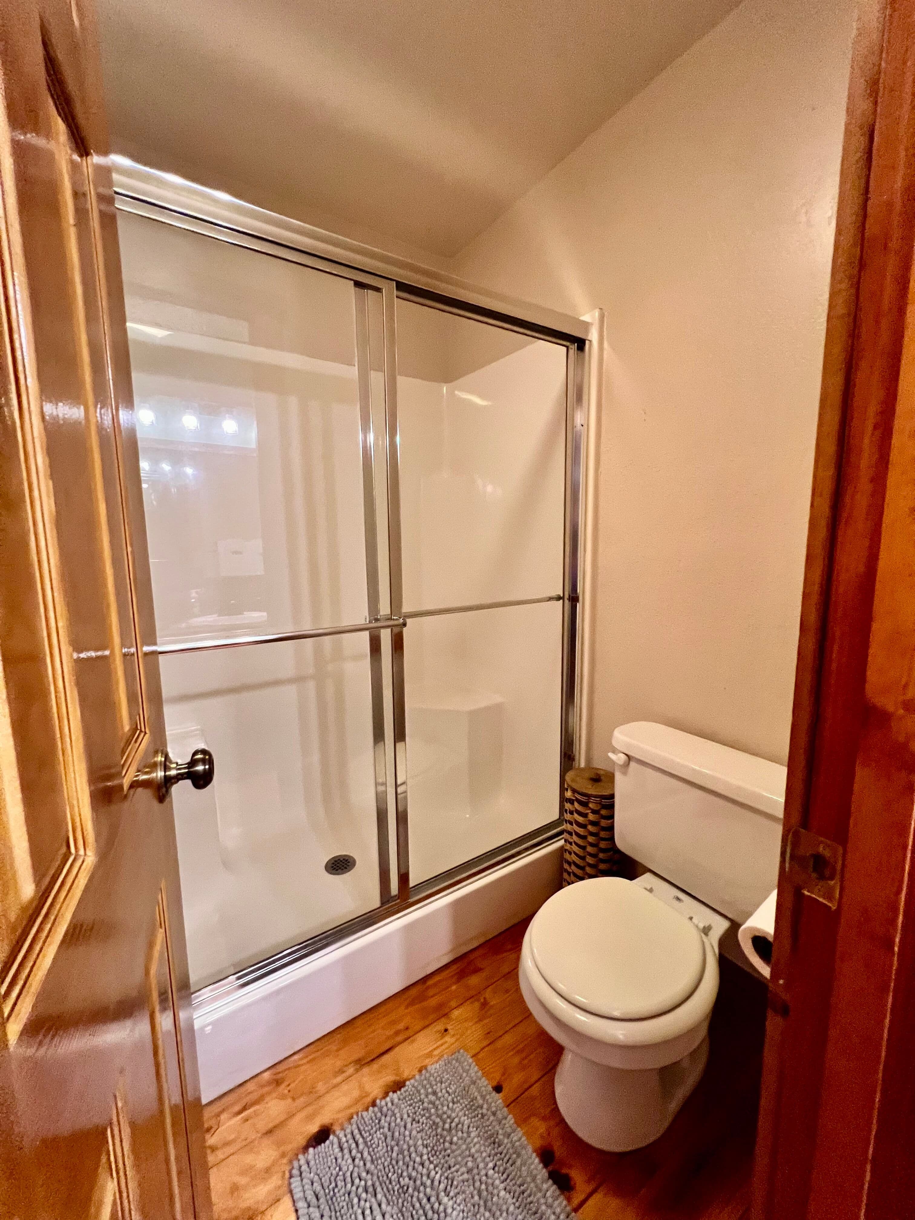 View of bathroom shows large shower with glass doors, toilet, and plush white towels hanging on rack