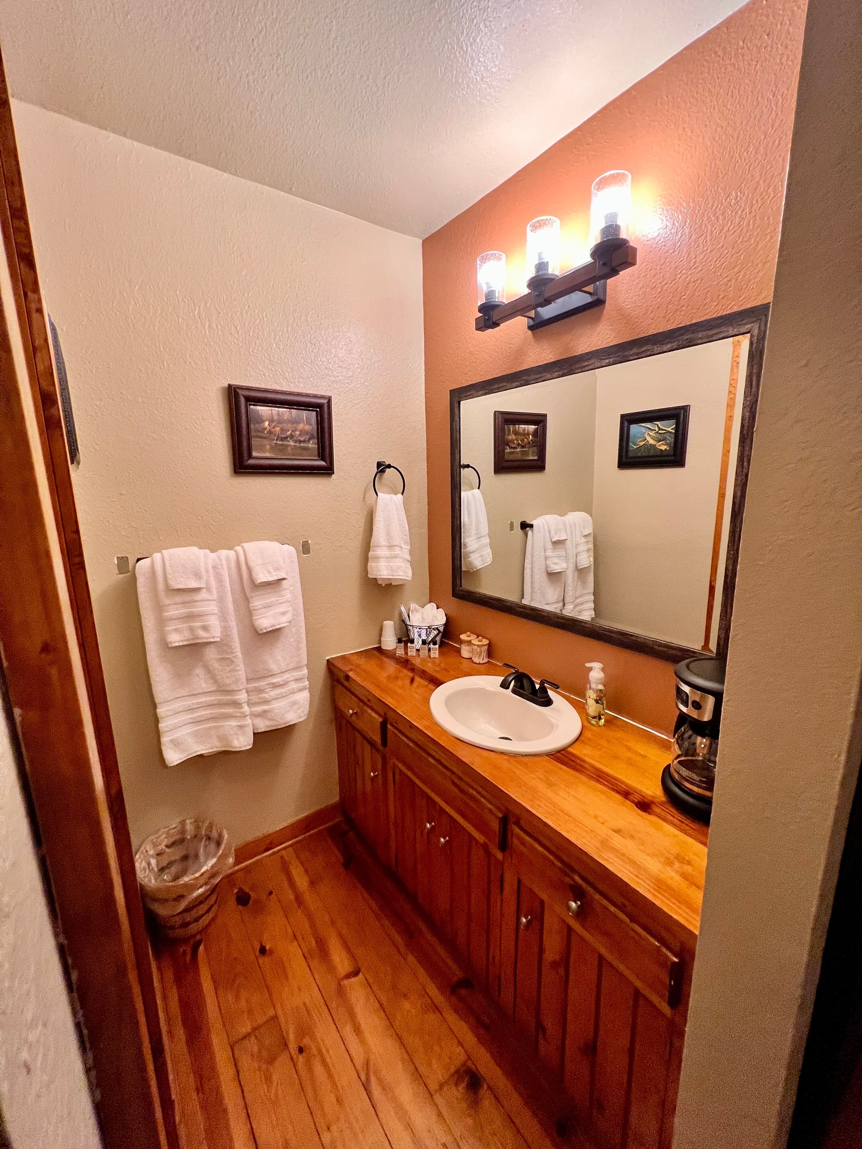 View of bathroom through doorway, beautifully stained wood vanity with sink, hardwood floors, plush white towelsHandcrafted log TV stand with drawers and shelves topped with flat-screen TV
