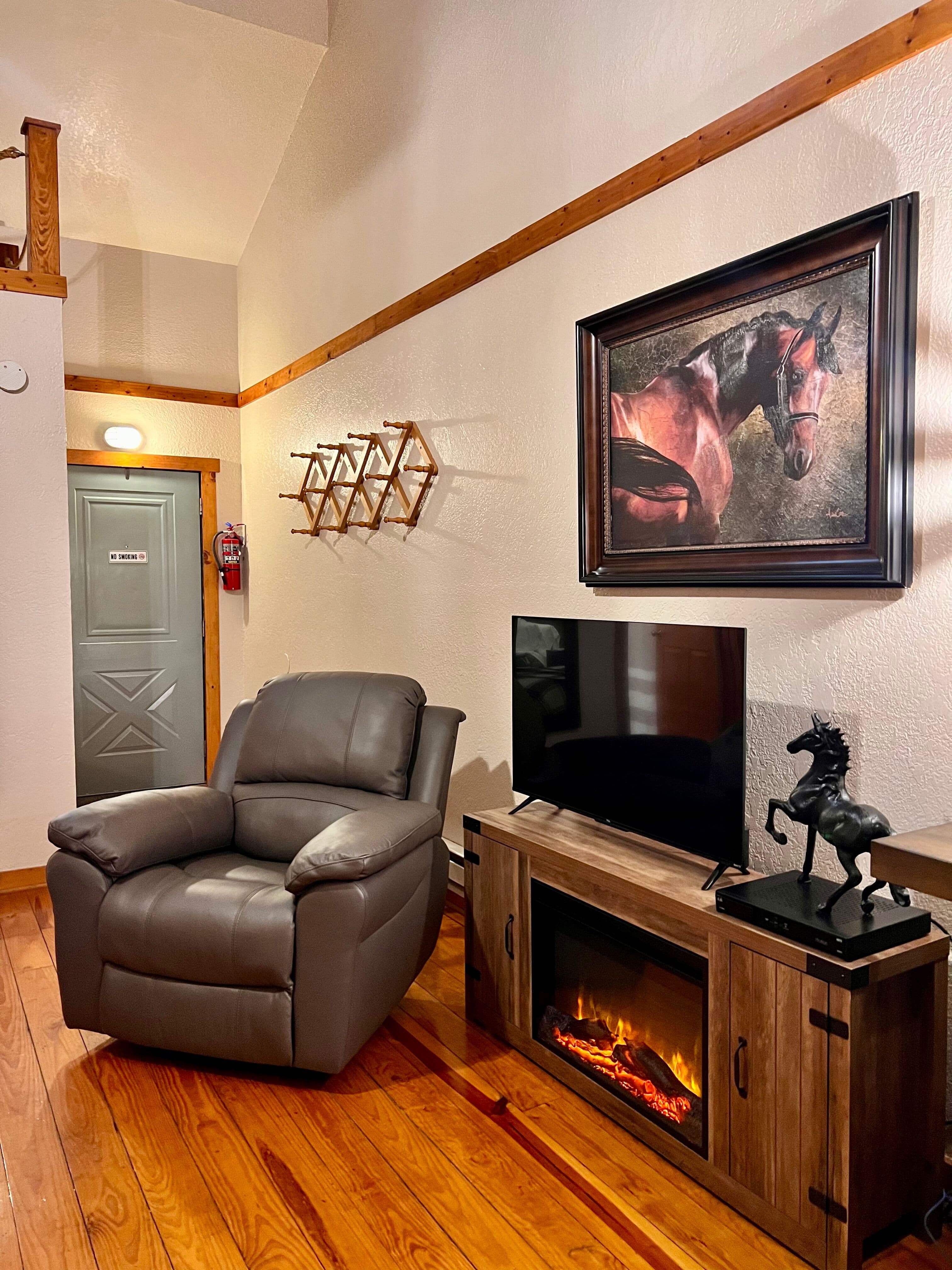 Comfortable sitting area with hardwood floor, leather recliner, electric fireplace console with flat-screen TV, and horse statue, framed horse painting on wall